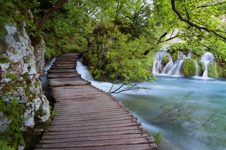 Beautiful view of waterfalls with turquoise water and wooden pathway through over water. Plitvice Lakes National Park, Croatia. Famous attraction, summer landscape.の写真素材