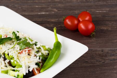 Traditional classic Shopska salad with tomatoes, peppers, cucumbers and cheese in white dish on grey wooden table. Bulgarian cuisine, Balkan cultureの写真素材