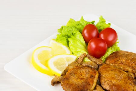 Pork fillet steak with cherry tomatoes, lemon and a lettuce in white dish on white background.の写真素材