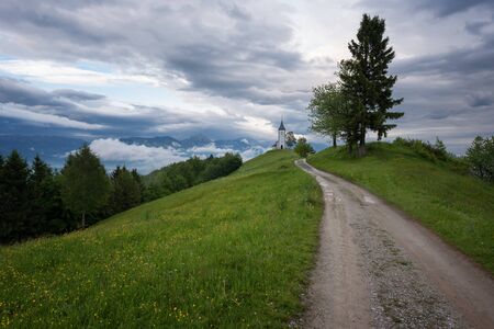 Jamnik church on a hillside in the spring, foggy weather at sunset in Slovenia, Europe. Mountain landscape shortly after spring rain. Slovenian Alps.の写真素材