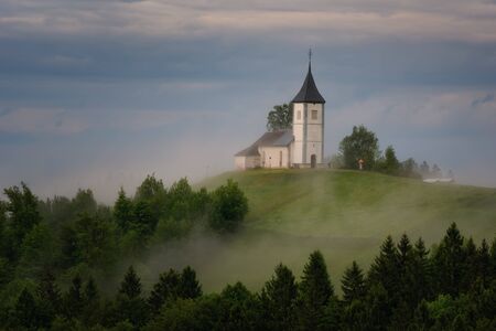 Jamnik church on a hillside in the spring, foggy weather at sunset in Slovenia, Europe. Mountain landscape shortly after spring rain. Slovenian Alps.の写真素材