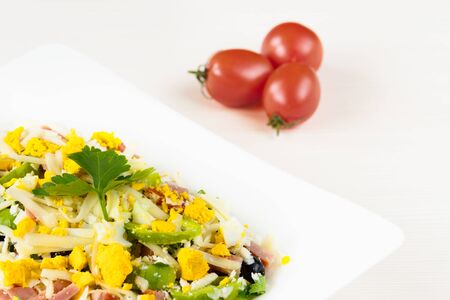 Traditional Bulgarian Shepherd salad with tomatoes, peppers, cucumbers, mushrooms, ham, cheese and eggs in white dish on white wooden table. Bulgarian cuisine, Balkan cultureの写真素材