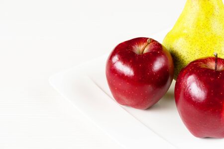 Red apples, green pear in white plate on white wooden board.の写真素材