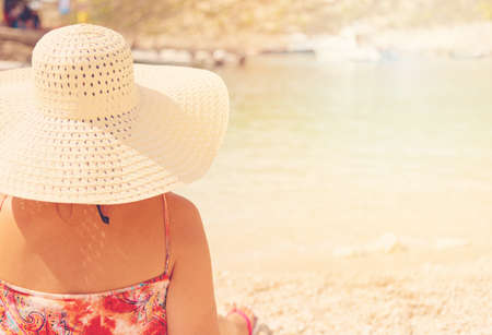Young woman in summer dress and hat standing on sand and looking to a the port of Porto Vromi, Greece.の写真素材