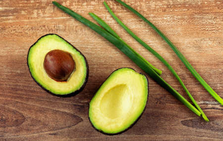 Close-up photo of fresh sliced avocados, brown seeds visible on brown wooden background. Top view. Copy space. Vegetarian food concept, vintage style, avocado background.の写真素材