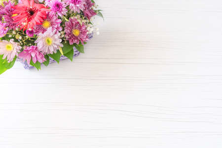 Beautiful bouquet of bright flowers in basket on white wooden background.の写真素材