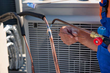 HVAC technician is working on air conditioner units on a roof of new industrial building. Croped image of HVAC technician who welds joint of copper pipe air conditioner.の写真素材