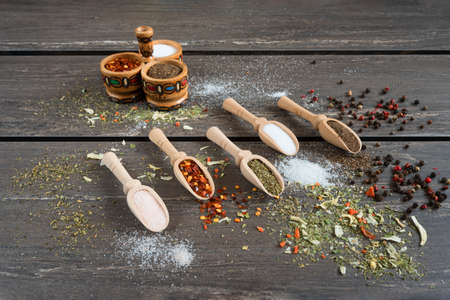 Various of spices and in wooden spoons. Flat lay of spices ingredients chilli, salt, himalayan salt, savory and black pepper on grey wooden board.の写真素材
