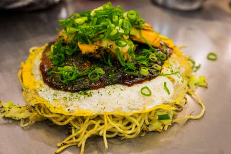 Okonomiyaki the traditional food from kansai Osasaka Japan contains with egg noodle half fried egg and some ingredients.の写真素材