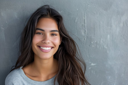 smiling young latin woman with grey wall backgroundの素材