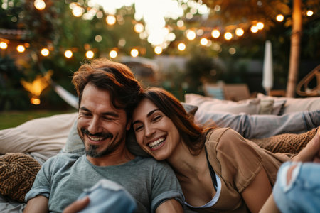 Happy couple man and woman enjoying in movie night with friends in backyardの素材