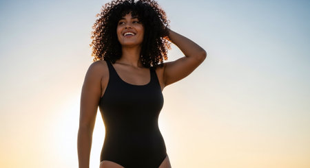 Portrait of young african american woman in swimsuit smiling and looking away on sunsetの素材