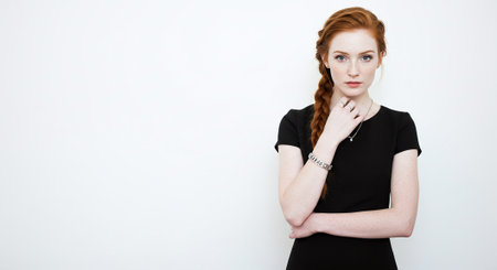 Portrait of beautiful young redhead woman with freckles and freckles, wearing black dress, looking at camera, standing over white background.の素材