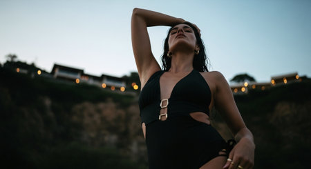 Sexy brunette girl in black swimsuit posing at sunset on the beachの素材