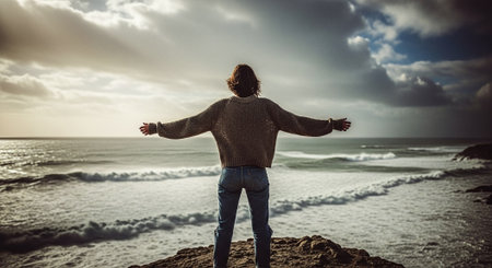 Man standing on a cliff with his arms outstretched looking at the oceanの素材