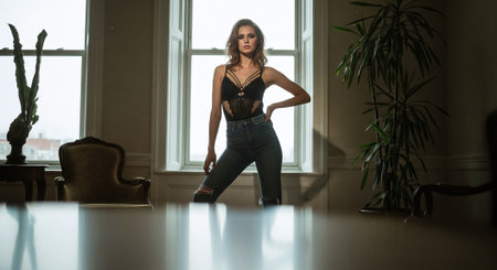 Sexy young woman in jeans and black top posing in a roomの素材