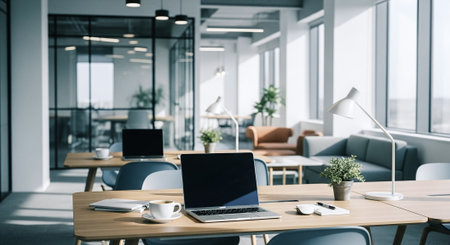 A modern office interior featuring desks with laptops, stylish lamps, and plants, large windows allowing natural light, and a cozy seating areaの素材