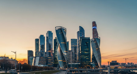 A modern city skyline at sunset, featuring tall skyscrapers with unique architectural designs, reflecting warm colors of the skyの素材