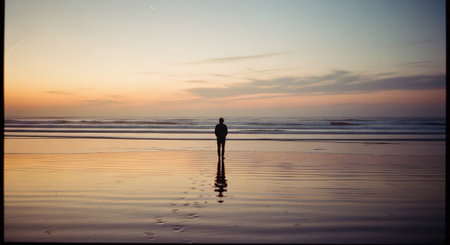 Silhouette of a man standing on the beach at sunrise.の素材