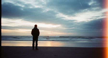 Silhouette of a man standing on the beach at sunset.の素材