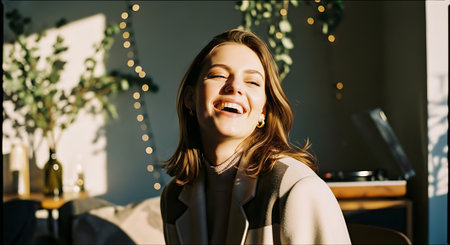 A young woman laughing joyfully in a cozy room with string lightsの素材