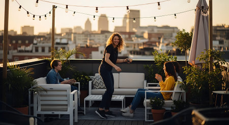 Friends socializing on a rooftop patio with a city skyline view at sunsetの素材