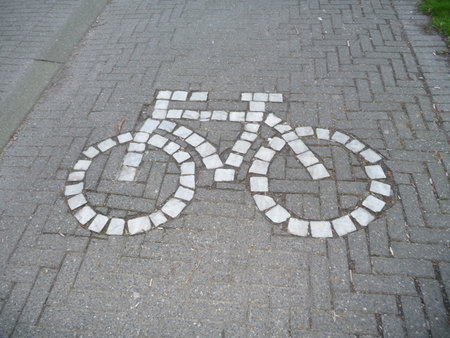 A large mosaic symbol of a bicycle made of light stone bricks set into a dark gray brick pathway.の写真素材