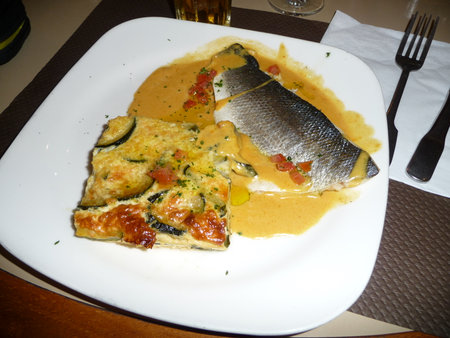 Fried fish with sauce and zucchini omlet on a white plate in a restaurantの写真素材