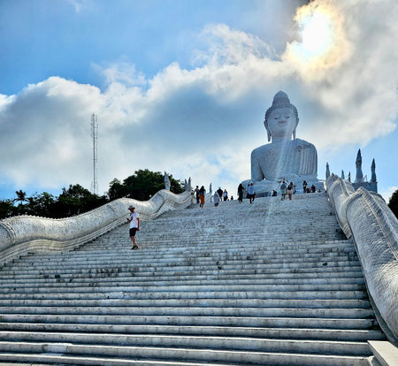 March 29, 2023, Phuket, Thailand. Famous Big Buddha statue in Phuket, Thailand. Tourists climbing white marble stairs under blue cloudy sky.のeditorial素材