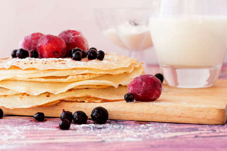 Pancakes with black currant and plum on wooden plate closeup.の写真素材