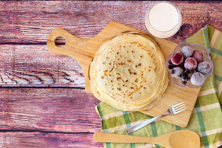 Stack of fresh russian pancakes. Pancakes with milk and berries on wooden background. Top view.の写真素材