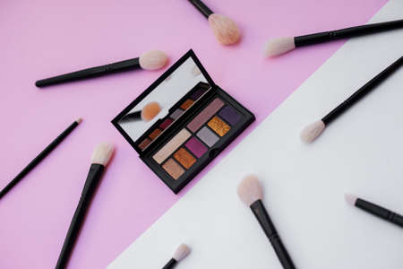 Side view of colorful metallized eyeshadow pallete and natural makeup brushes on white and pink background. Especially for beauty and fashion brands. Content for girly blogs.の写真素材