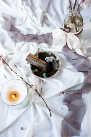Composition with peruvian palo santo holy wood on handmade ceramic plate, white candle and bottle with banch of blooming almand tree. Esoteric objects for meditation. Antistress and relaxation.の写真素材