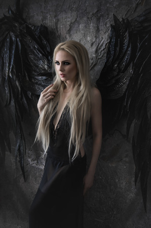 Beautiful blond woman in black dress with black wingsの写真素材