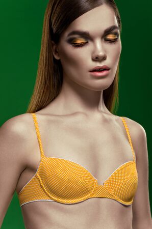 Beautiful tall brunette woman dressed in yellow lingerie with closed eyes on green backgroundの写真素材