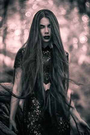 Young woman posing in black lace dress in dark forestの写真素材