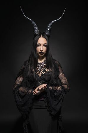 Young woman in black fantasy costume with big horns on dark backgroundの写真素材