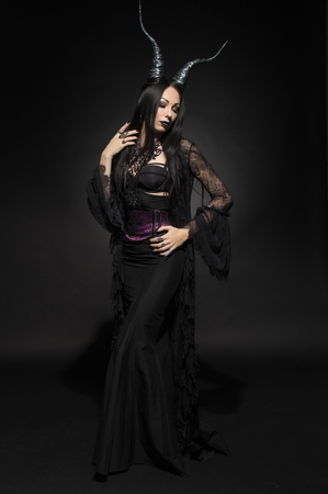 Young woman in black fantasy costume with big horns on dark backgroundの写真素材
