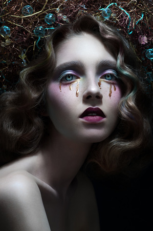 Fashion studio portrait of model with stylish haircut, and makeup with tears, black background, closeupの写真素材