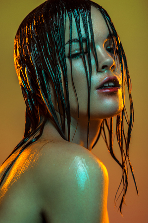 Closeup fashion portrait of beauty girl with studio makeup and wet hair, on orange backgroundの写真素材
