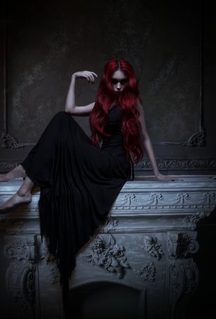 Beautiful red haired woman in black dress posing in gothic entourageの写真素材