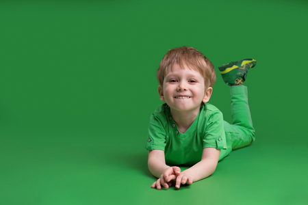 Happy boy in green clothes posing at camera against green backgroundの写真素材