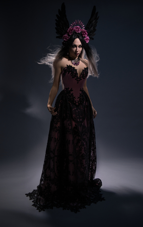 Full length view of charming brunette woman in rose crown posing on dark backgroundの写真素材