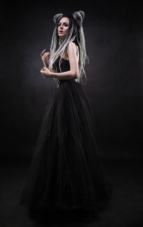 Woman with dreads and black gothic dress posing on dark backgroundの写真素材