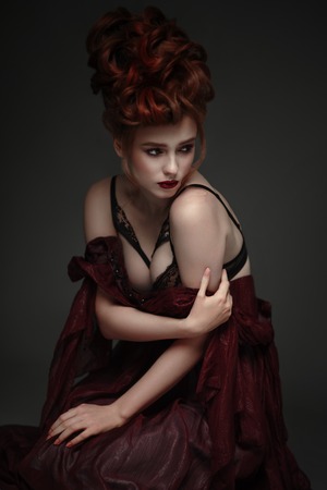 Portrait of woman with baroque hairstyle and fancy lace lingerie posing on dark backgroundの写真素材