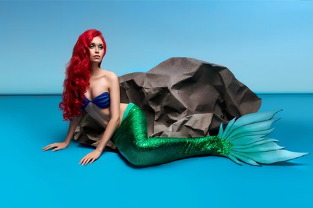 Mermaid with red hair resting near stone on blue backgroundの写真素材