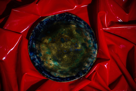 Handmade brown plate laying on glossy red clothの写真素材