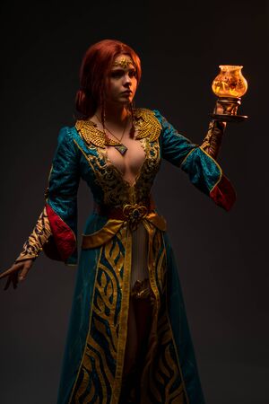 Beautiful redhead woman in cosplay costume with magic lamp on grey backgroundの写真素材
