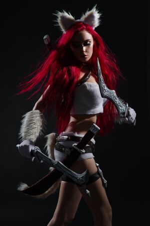 Sexy redhead woman in cosplay costume of warrior cat with swords posing on dark backgroundの写真素材