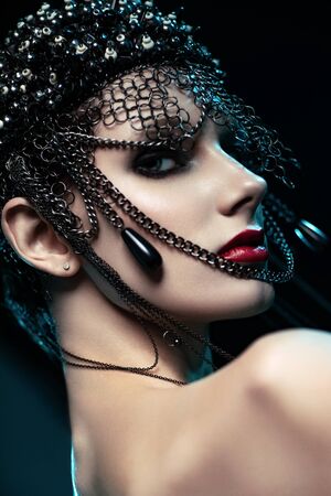 Portrait of attractive brunette woman in designer headdress with chains posing on dark studio backgroundの写真素材